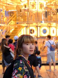 Portrait of young woman against illuminated carousel