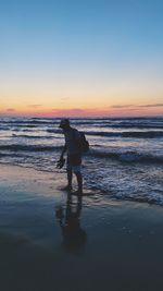 Man standing on beach against sky during sunset