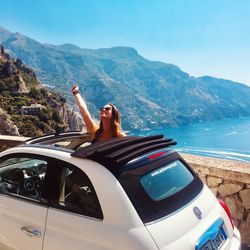 Woman in car by mountains against sky