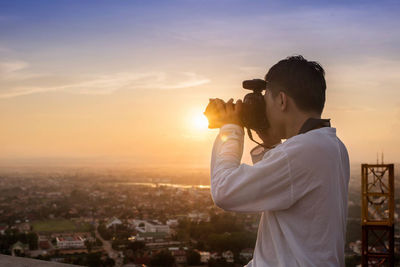 Man photographing cityscape against sky during sunset