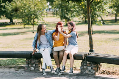 A group of teenage girls sitting and high-fiving with a laptop in the park. meeting on a training 