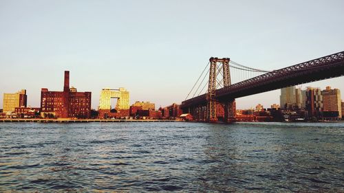 Bridge over river by buildings in city against clear sky