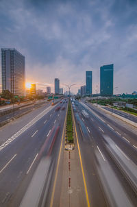 Road by buildings against sky during sunset in city