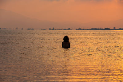 Rear view of silhouette woman on sea against sky during sunset