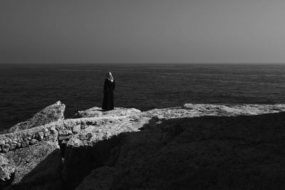 Rear view of woman standing on rock formation by sea against sky