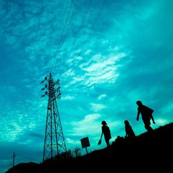 Low angle view of silhouette electricity pylon against blue sky