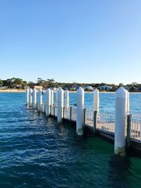 Wooden posts in sea against clear blue sky