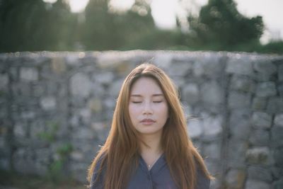 Young woman with eyes closed standing against stone wall