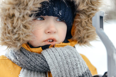 Close-up of a baby in a winter red jacket with a fur hood. looks away