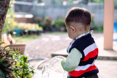 Adorable asian toddler boy plays and enjoys having fun watering garden flowers and lawn 