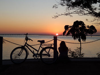 Silhouette people riding bicycle on beach against sky during sunset