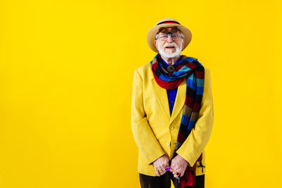 Senior man standing against yellow background