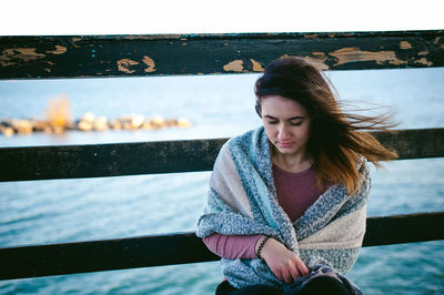 Thoughtful young woman sitting on pier over sea