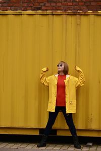 Portrait of young woman standing against yellow wall