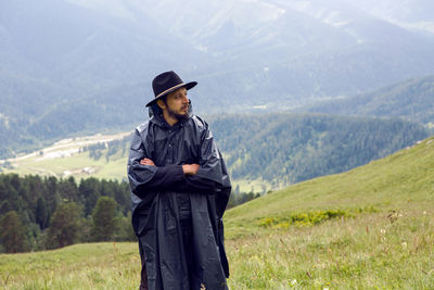 Man with a beard shepherd standing in the mountains in a black raincoat in the rain