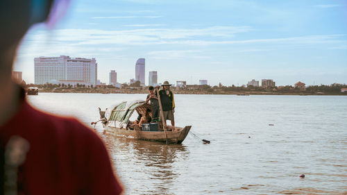 People in wooden boat on river against sky