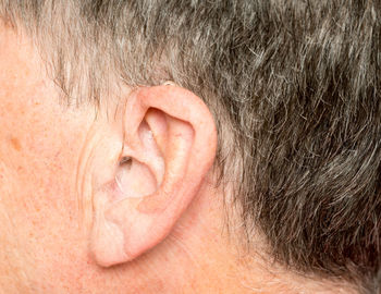 Close-up of senior man holding hearing aid against beige background