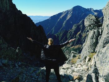 Rear view of woman with arms raised standing on mountain against sky