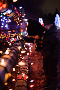 Boy in warm clothing standing by illuminated lights
