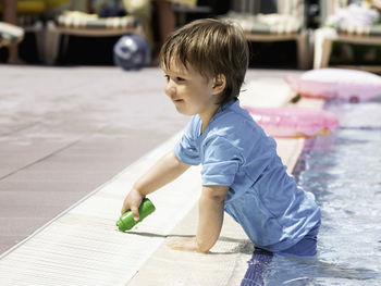 Toddler baths in swimming pool. boy in blue swimwear playing in paddling pool. vacation in hotel.