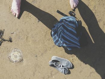 Low section of person standing by bag and shoes on beach during sunny day