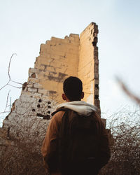 Rear view of man standing by building against sky