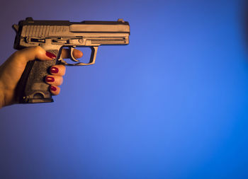 Cropped hand of woman holding gun against blue background