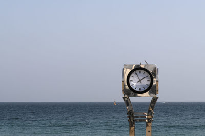 Clock on sea against clear sky