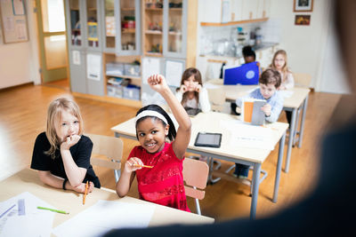 Smiling student with hand raised sitting in classroom