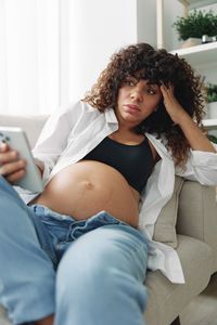 Portrait of young woman using mobile phone while sitting on bed at home