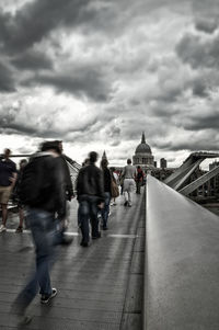 People walking in city against cloudy sky