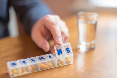 Midsection of man taking medicines from pill organizer at home