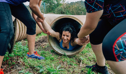 Friends pulling woman from pipe in forest