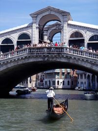 Man in gondola at grand canal with people standing on rialto bridge