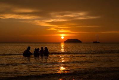 Silhouette people in sea against sky during sunset