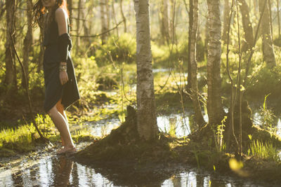 Midsection of woman standing amidst trees in forest