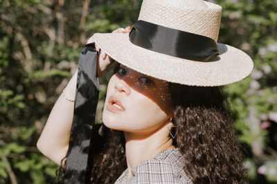 Portrait of young woman holding hat sitting at park