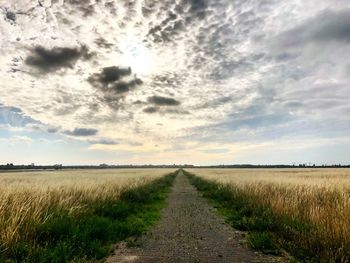 Dirt road amidst field against sky