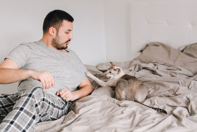 Young man with cat lying on bed at home