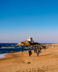 People on beach against clear blue sky