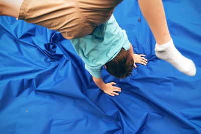 High angle view of boy performing handstand on blue fabric in yard