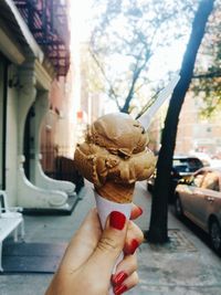 Cropped hand holding ice cream cone on sidewalk