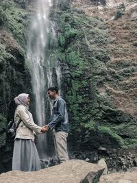 Couple holding hands while standing against waterfall