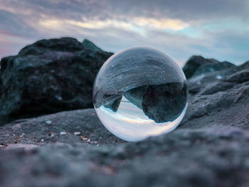 Close-up of crystal ball on rock at beach against sky