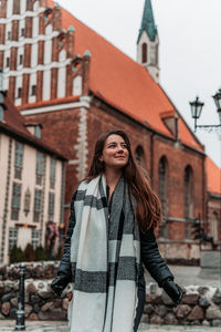 Portrait of young woman standing against wall in city