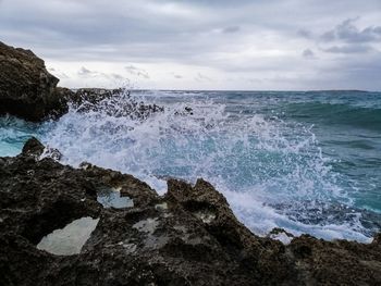 Waves splashing on rocks at shore against sky