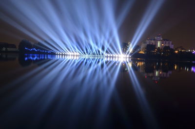 Illuminated city by river against sky at night