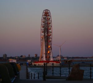 Ferris wheel by pier against clear sky at sunset