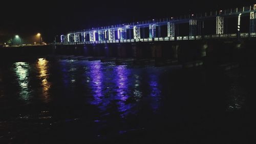 Illuminated bridge over river in city at night