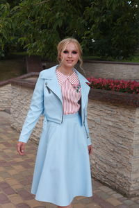 Portrait of young woman in dress standing on footpath against trees at park